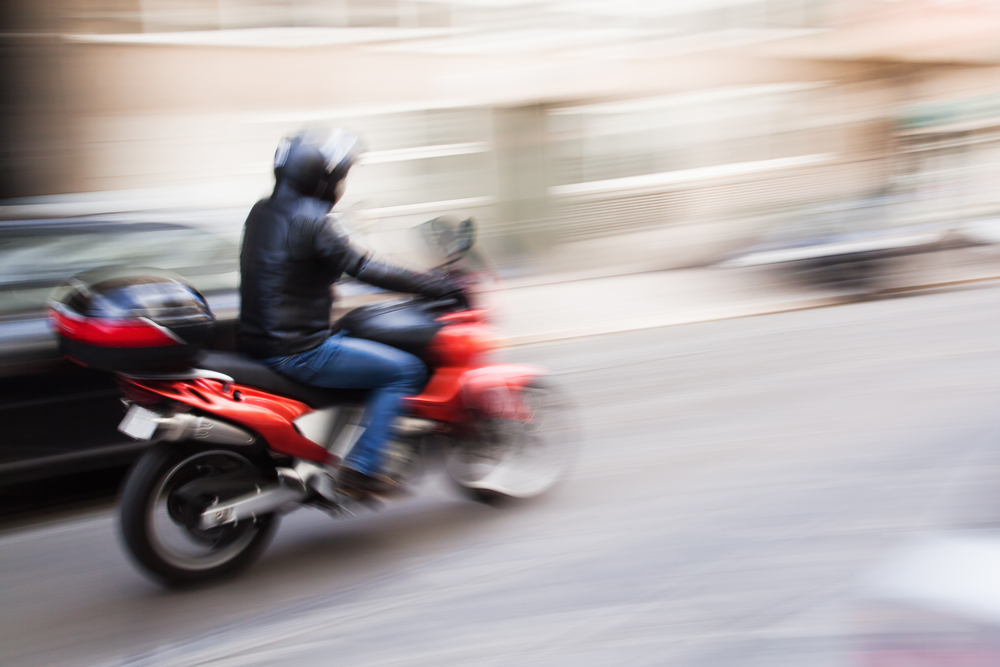 An unfocused image of a motorcyclist driving quickly through a city centre.