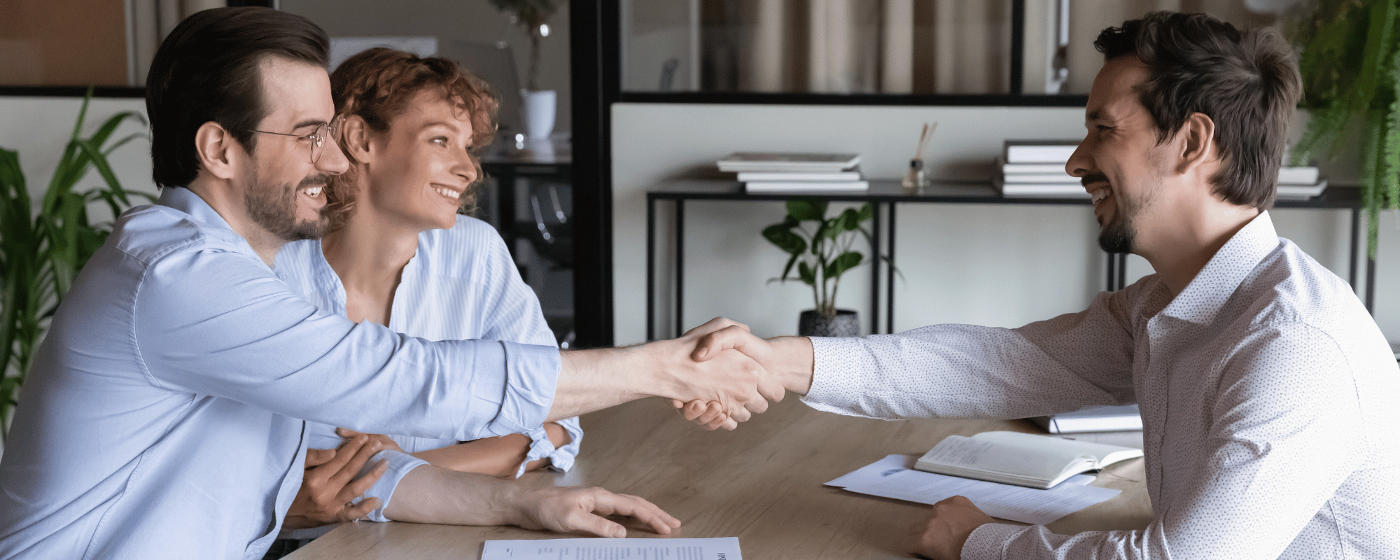 A smiling young couple and a solicitor shaking hands.