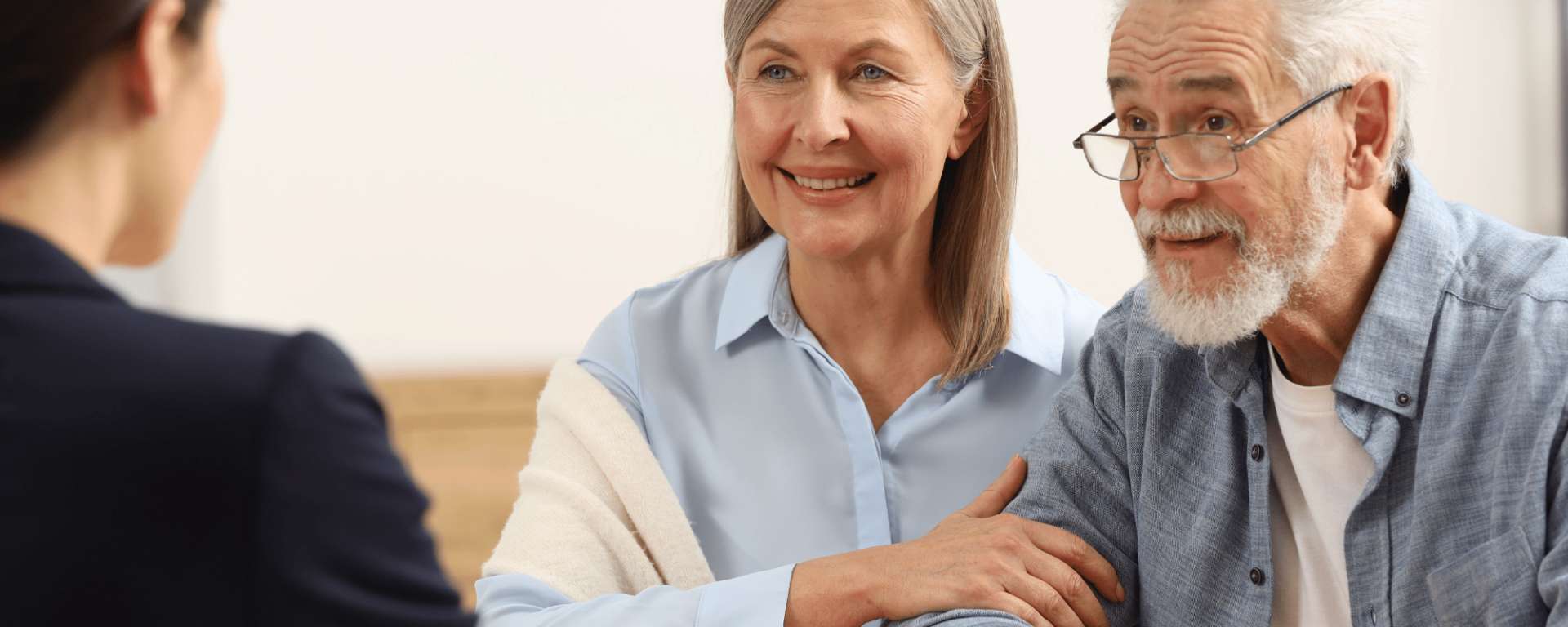 A smiling elderly couple receiving advice from a solicitor on Wills and Trusts.