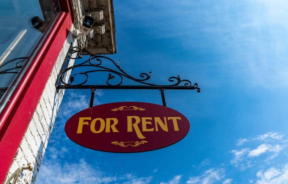 A Guide to Landlords Responsibilities & Legal Obligations in England A "for rent" sign hanging on a building, taken from a low angle with a blue sky background