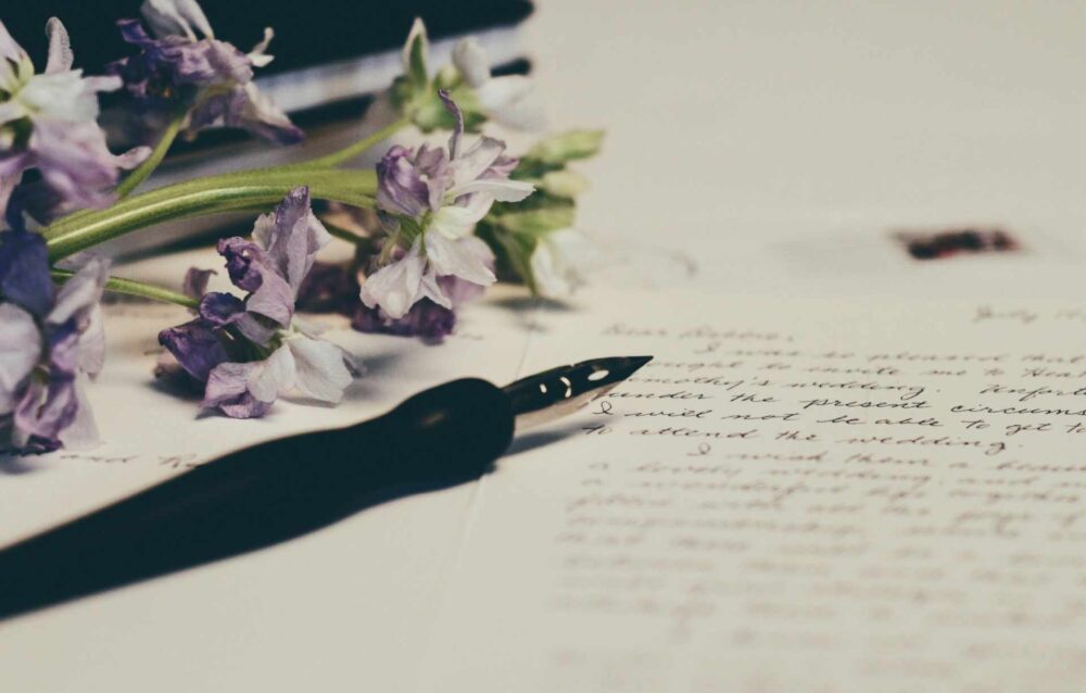 How Can You Find Out if Someone Has a Will and How to Get a Copy Online A stem of purple flowers and a calligraphy pen resting upon a handwritten Will document.