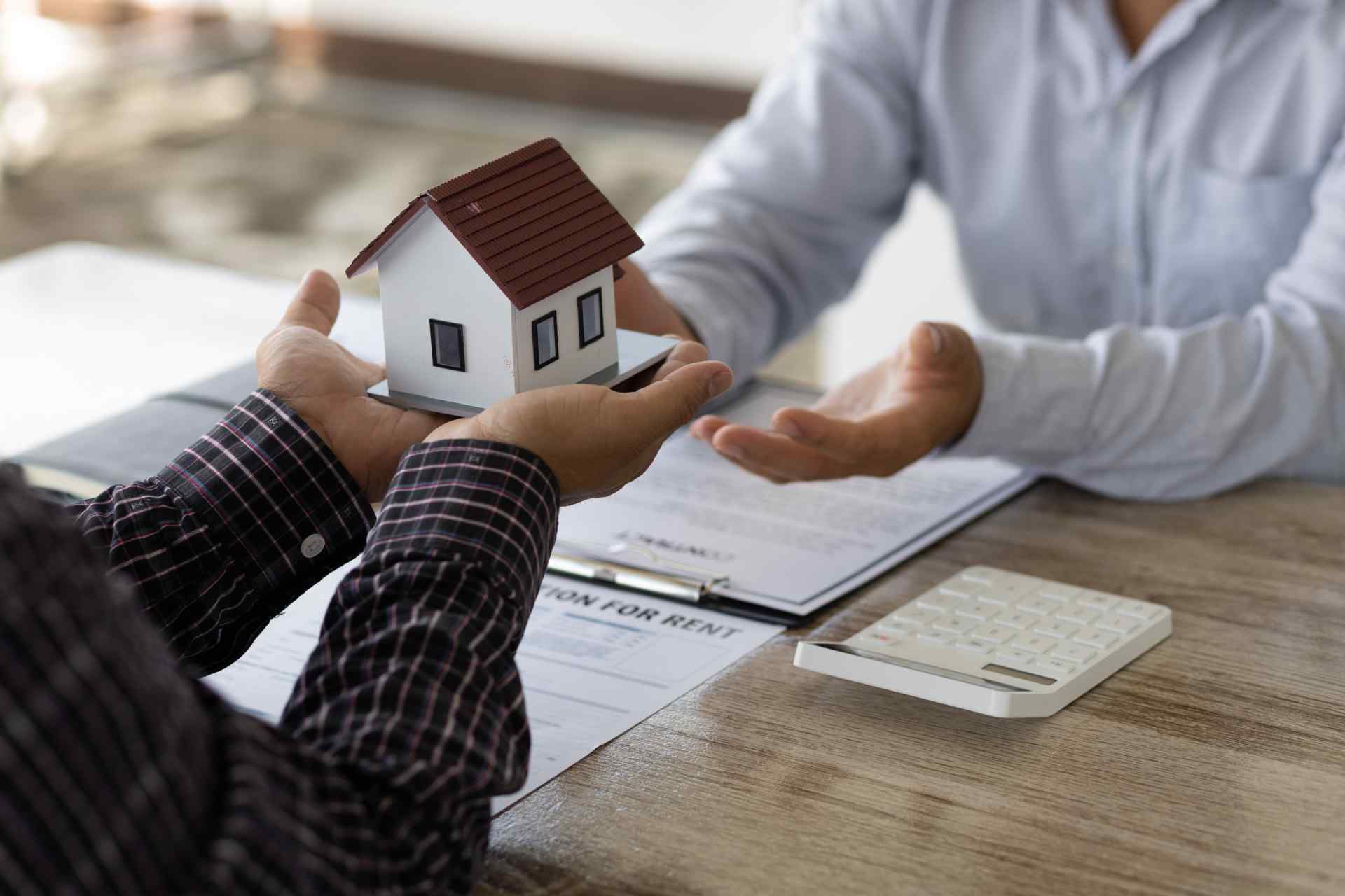 A man passes a small wooden model of a house to another man