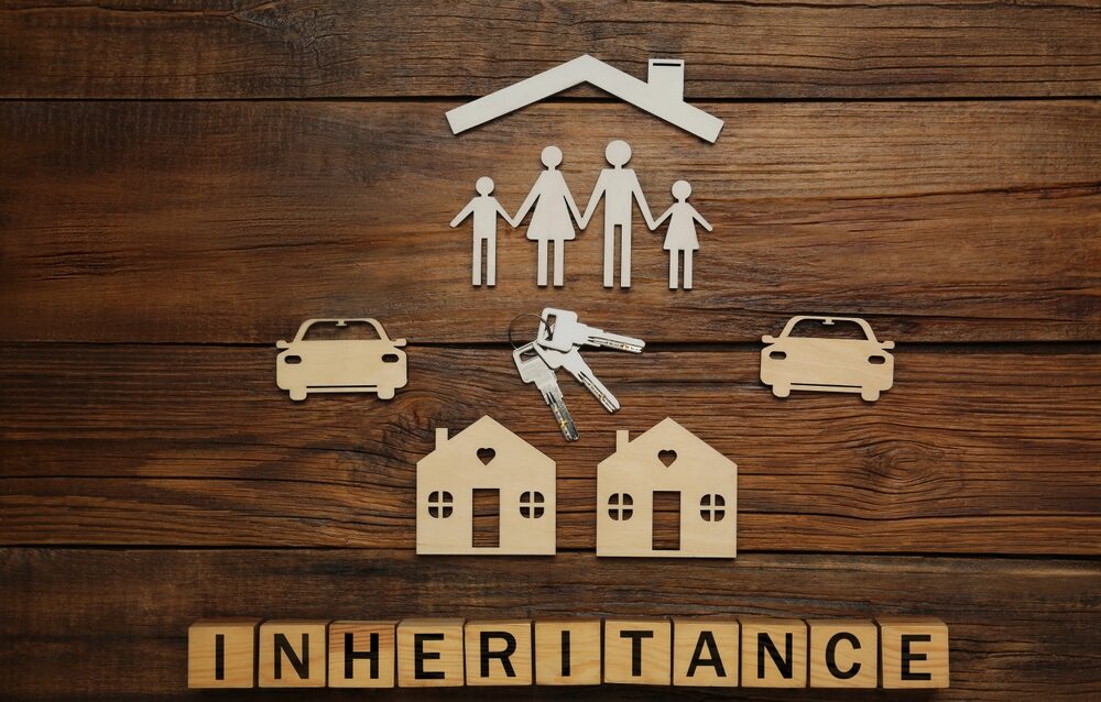 Inheritance-Tax-Changes wooden cut outs of a family, houses and two cars with "inheritance" spelt out underneath in building blocks.