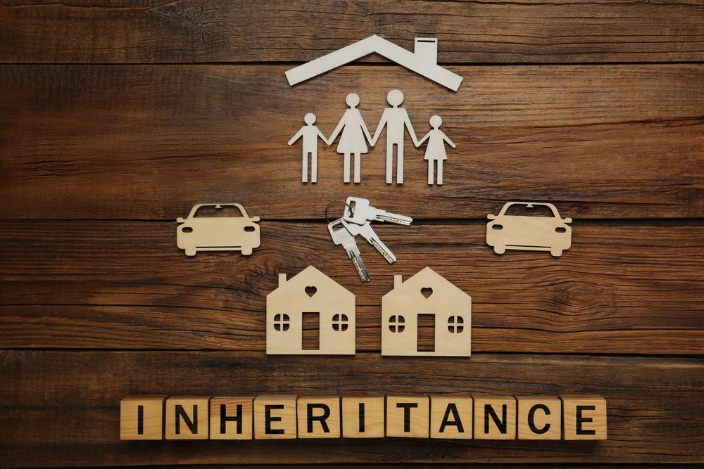 wooden cut outs of a family, houses and two cars with "inheritance" spelt out underneath in building blocks.