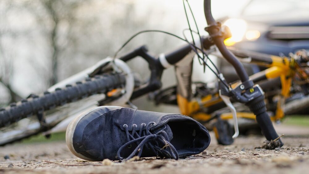 A bicycle lies on the ground with a car and its headlights visible in the background.