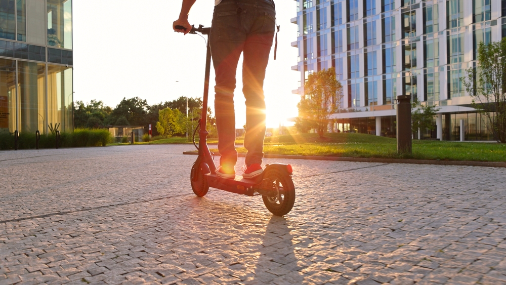 Person on an electric scooter at sunset near modern buildings.