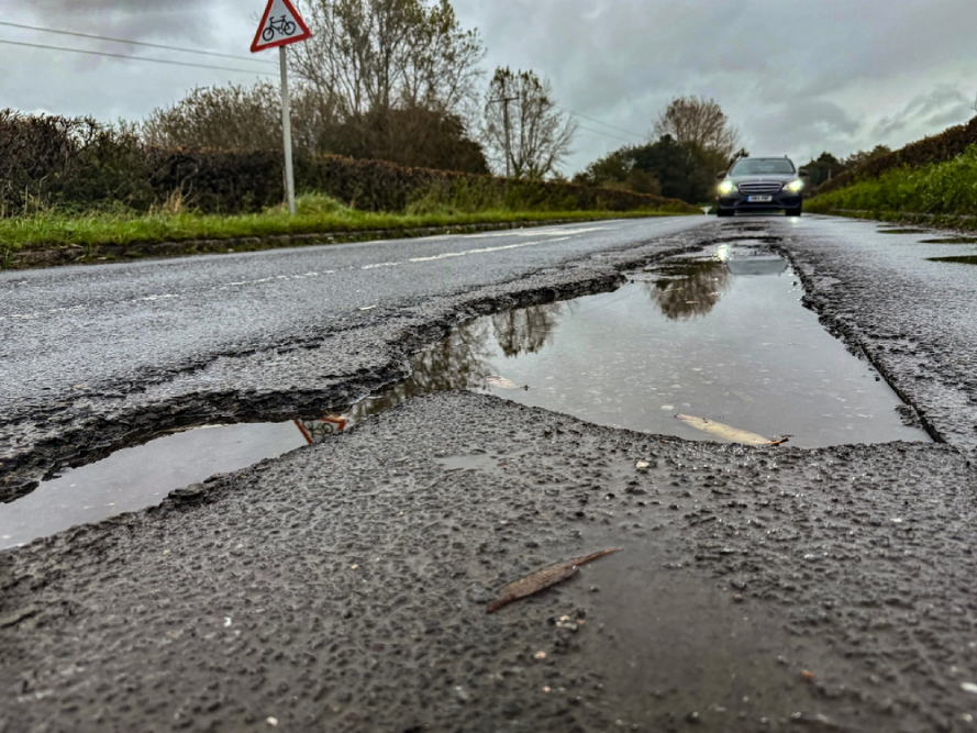 a image taken from the floor of a road with potholes in the rain with a car in the background