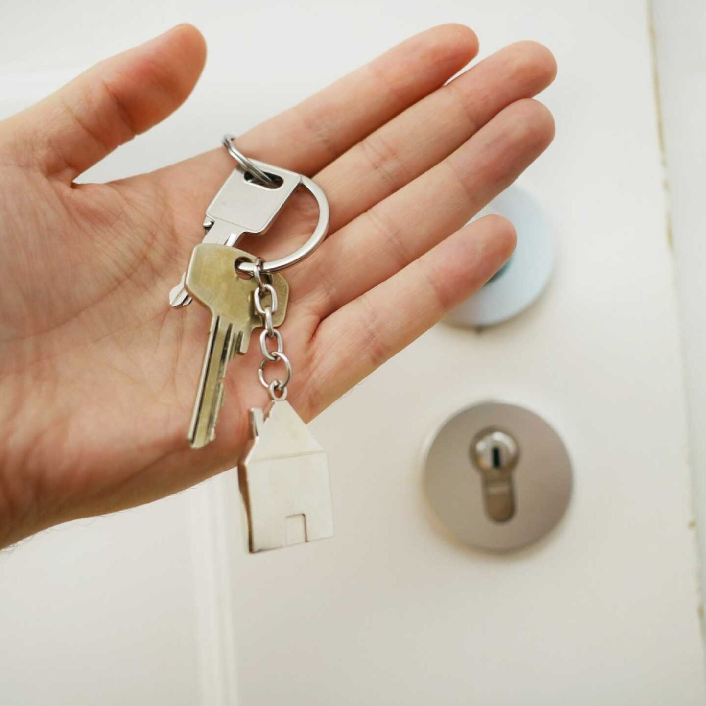 New Home A hand holding house keys next to a locked front door.